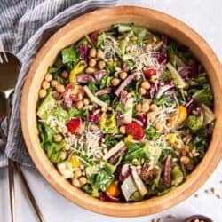 Italian chopped salad in a wood salad bowl next to a small bowl of pine nuts.