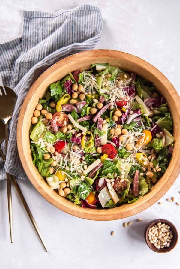Italian chopped salad in a wood salad bowl next to a small bowl of pine nuts.