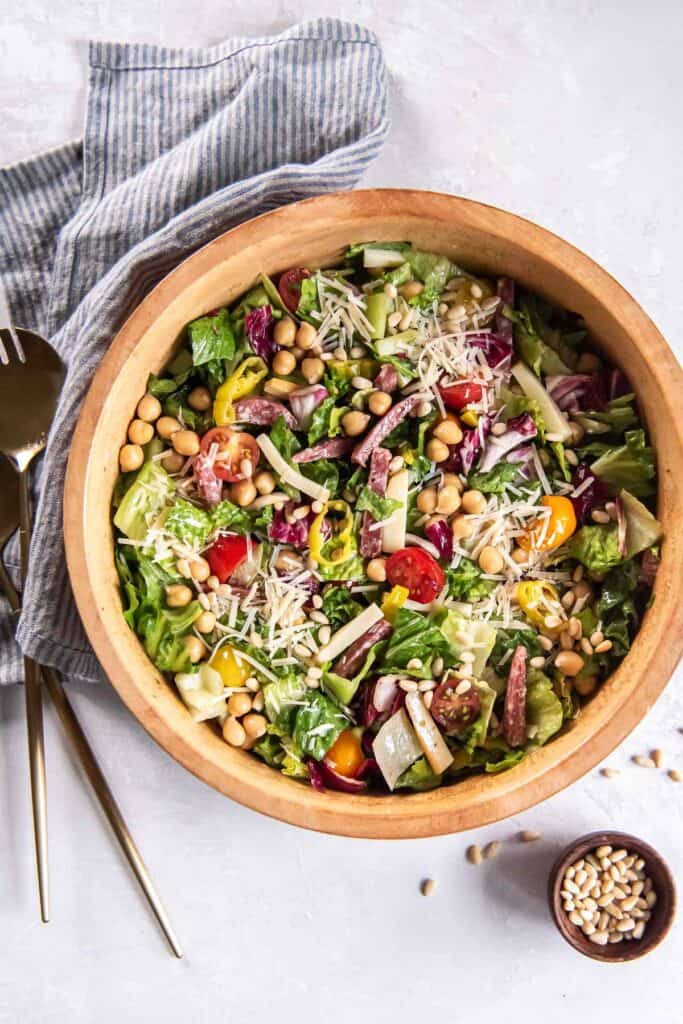 Italian chopped salad in a wood salad bowl next to a small bowl of pine nuts.