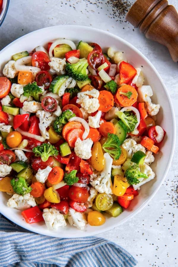 Marinated vegetables in a white bowl next to a blue kitchen cloth.