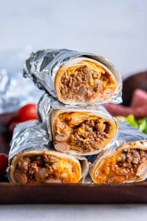 Foil wrapped beef and bean burritos sliced in half and stacked on a cutting board.