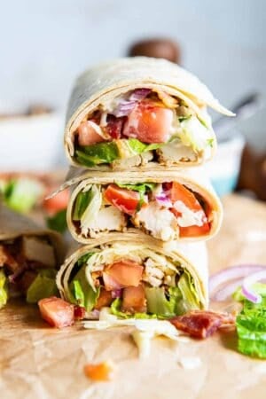 Chicken bacon ranch wraps sliced in half and stacked on a piece of parchment paper.