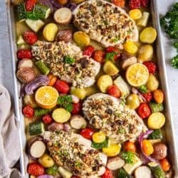 Greek feta stuffed chicken on a sheet pan with vegetables and lemon halves.