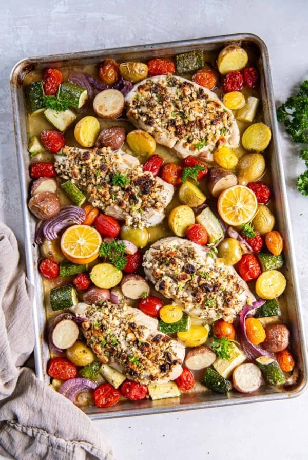 Greek feta stuffed chicken on a sheet pan with vegetables and lemon halves.