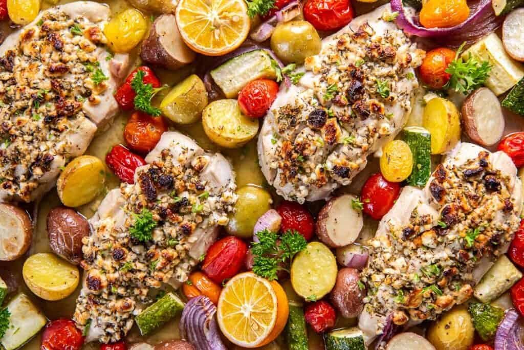 Chicen stuffed with feta on a baking sheet with roasted vegetables.