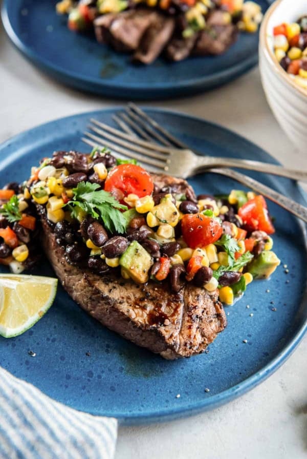 Forks resting on a blue plate with steak topped with corn black bean salsa.