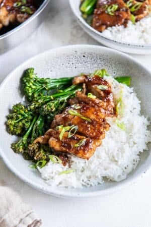 Sliced soy garlic chicken on top of white rice in a bowl with broccolini.