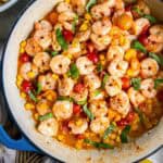 Shrimp scampi with tomatoes and corn in a blue skillet.