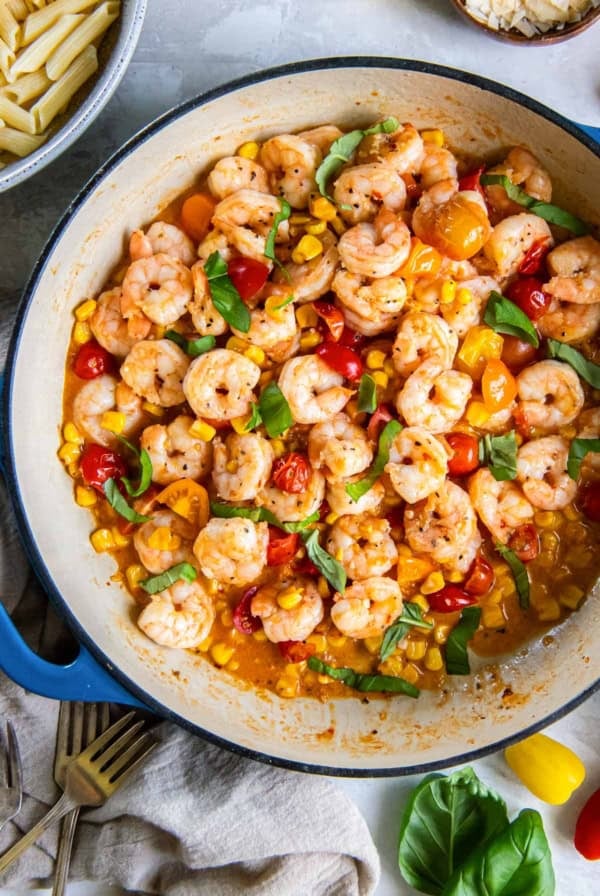 Shrimp scampi with tomatoes and corn in a blue skillet.