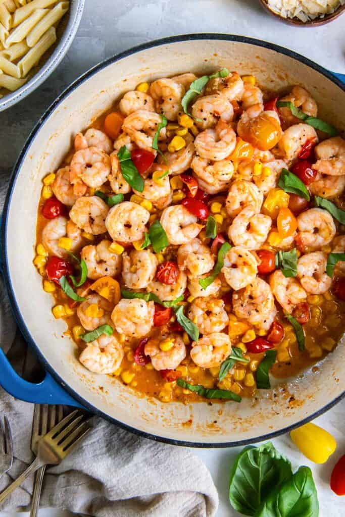 Shrimp scampi with tomatoes and corn in a blue skillet.