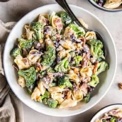 A spoon resting in a serving bowl filled with tortellini broccoli salad.
