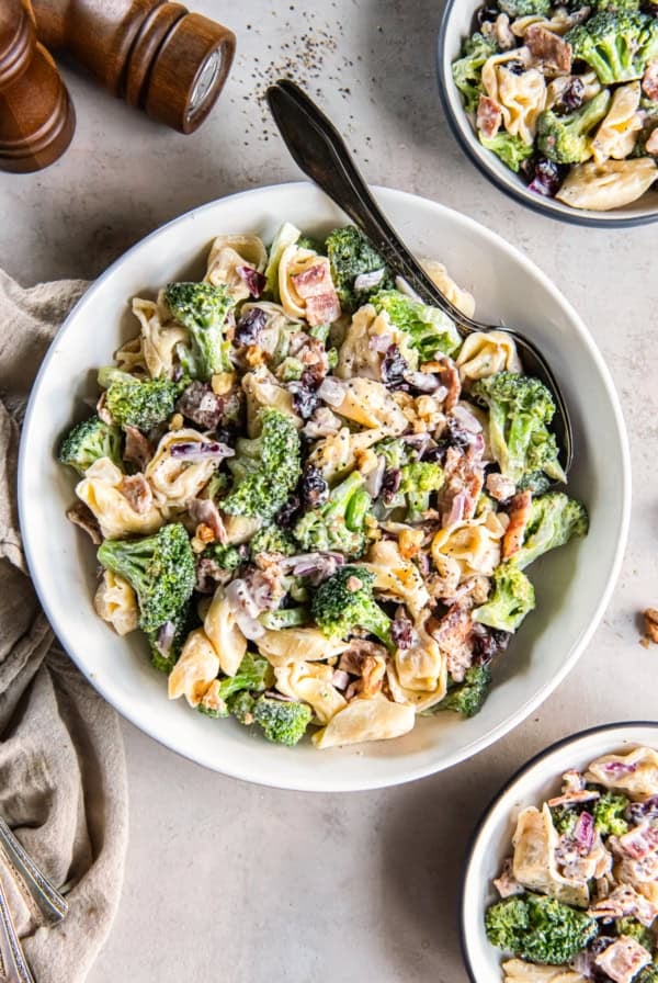 A spoon resting in a serving bowl filled with tortellini broccoli salad.