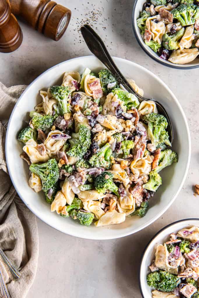 A spoon resting in a serving bowl filled with tortellini broccoli salad.