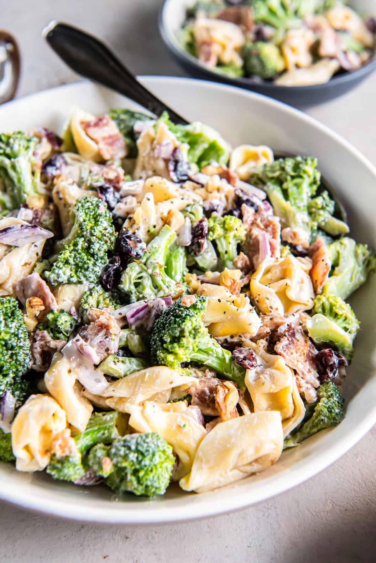 Tortellini broccoli salad with bacon and dried cranberries in a white serving bowl.
