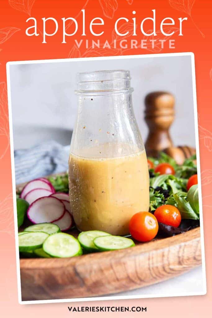 An open mason jar filled with apple cider vinaigrette on a wood platter with vegetables with text overlay.