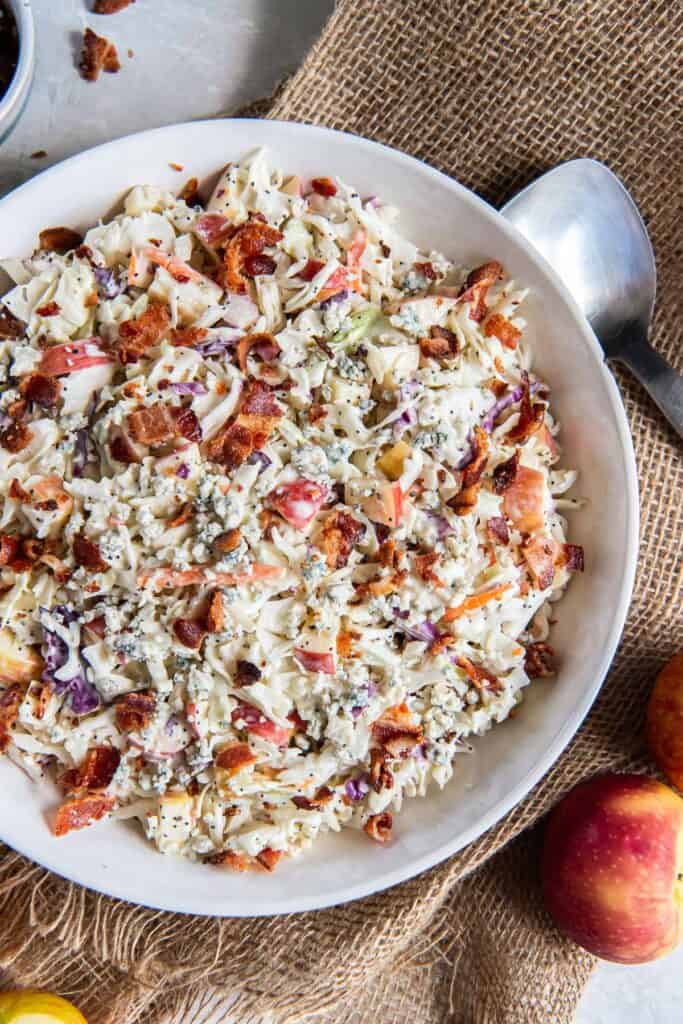 A large white bowl filled with apple coleslaw resting on a piece of burlap.