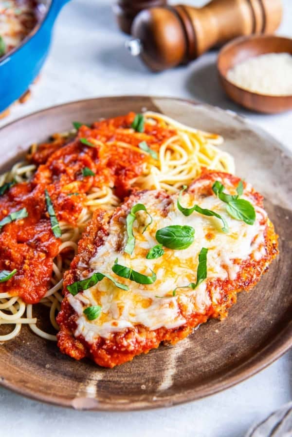Chicken parmesan on a plate with pasta and sauce.