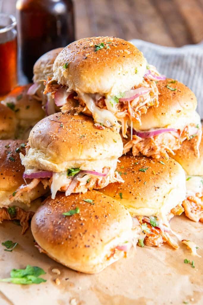 A stack of BBQ chicken sliders on parchment paper.