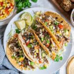 Chimichurri chicken tacos with corn, tomatoes, avocado, and cabbage on a white plate.