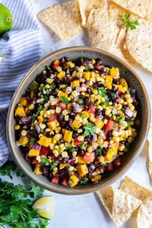 Mango corn salsa with black beans in a large serving bowl surrounded by tortilla chips.