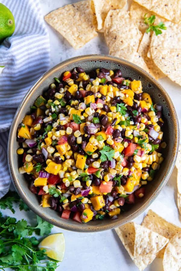 Mango corn salsa with black beans in a large serving bowl surrounded by tortilla chips.