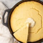 A spatula lifting a slice of cornbread from a cast iron skillet.