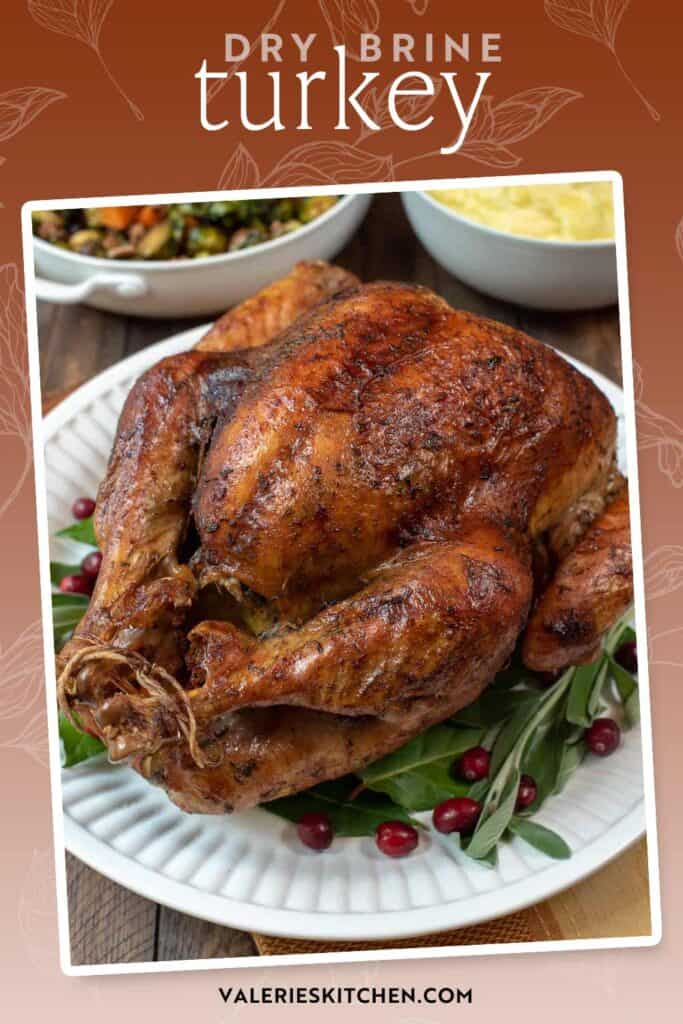A dry brined turkey on a white platter with fresh herbs and cranberries with text overlay.