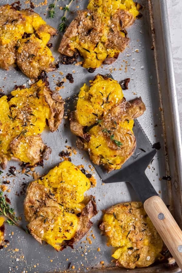 A spatula resting underneath a cirspy smashed potato on a baking sheet.