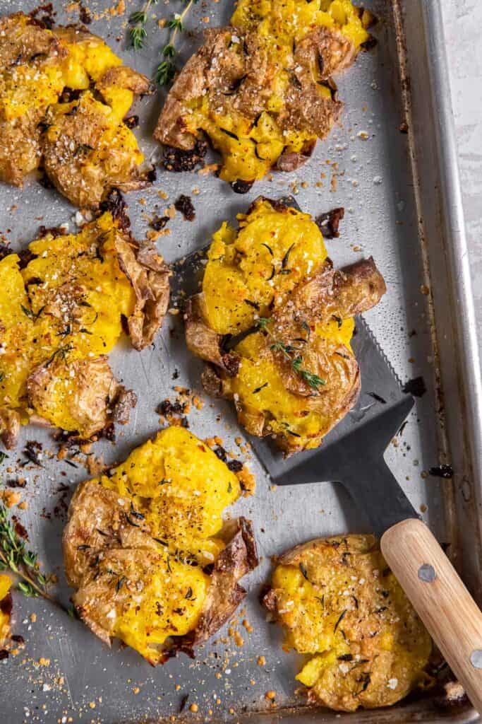 A spatula resting underneath a cirspy smashed potato on a baking sheet.