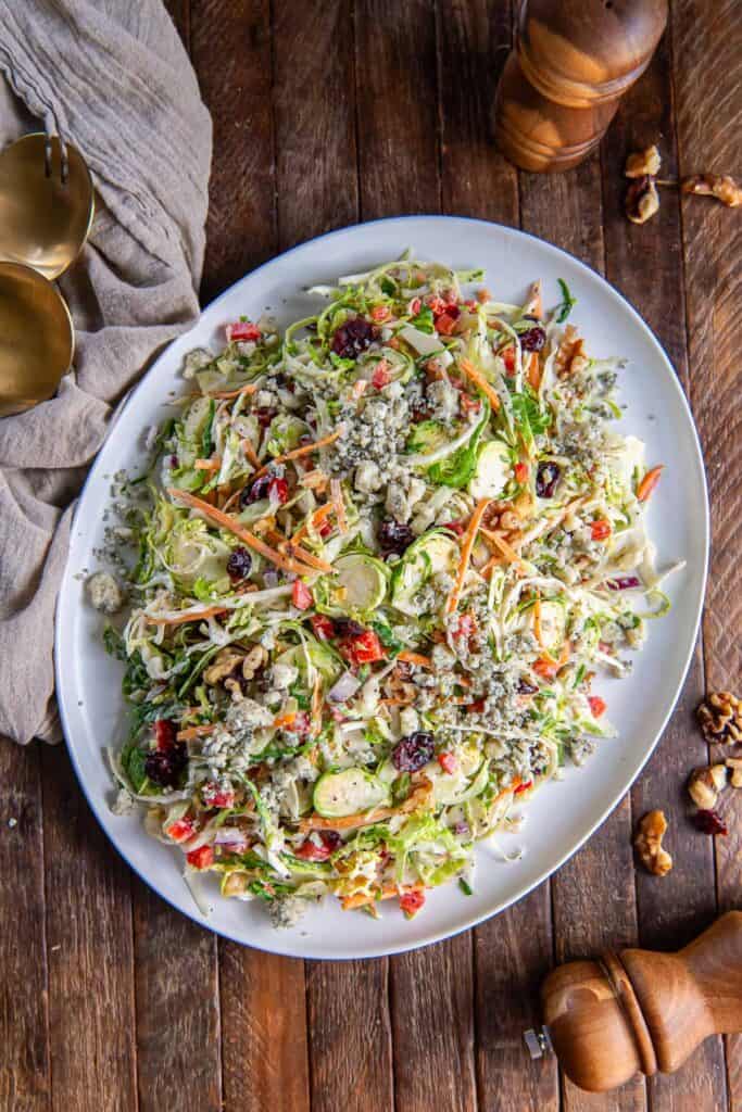 A platter of cranberry brussels sprouts coleslaw next to salt and pepper shakers and a kitchen cloth.