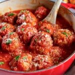 A spoon resting in a pot of Italian meatballs in marinara sauce.