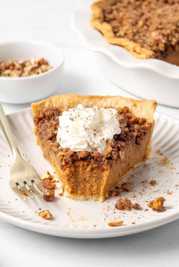 A slice of praline pumpkin pie topped with whipped cream with a bite missing.