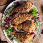 Roasted turkey drumsticks on a white platter with fresh herbs and cranberries.