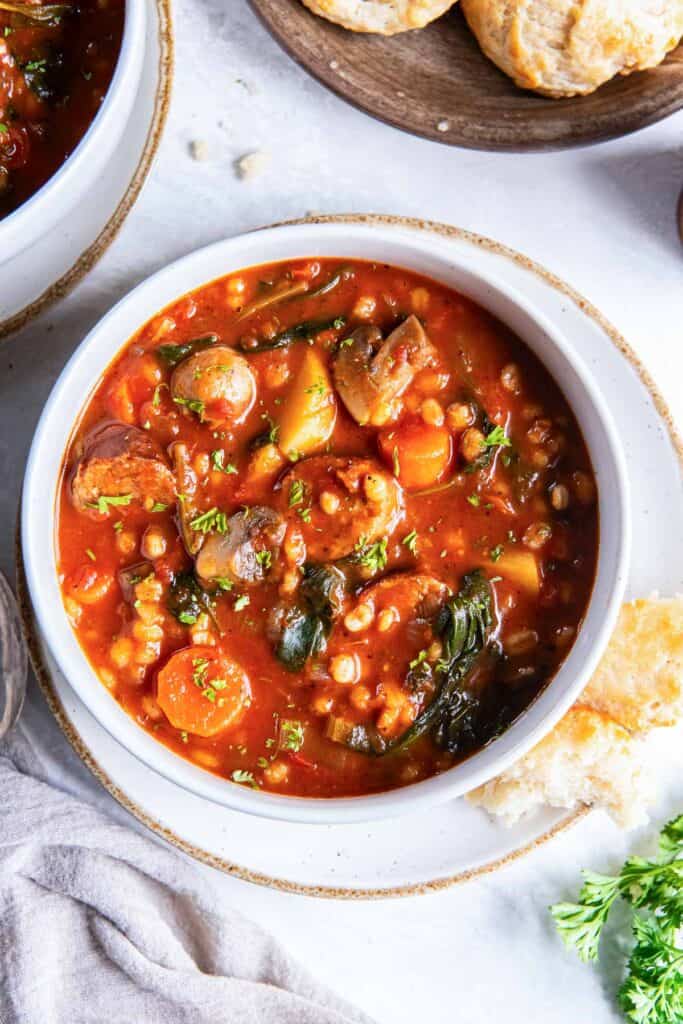 Sausage and barley stew with spinach in a white bowl.