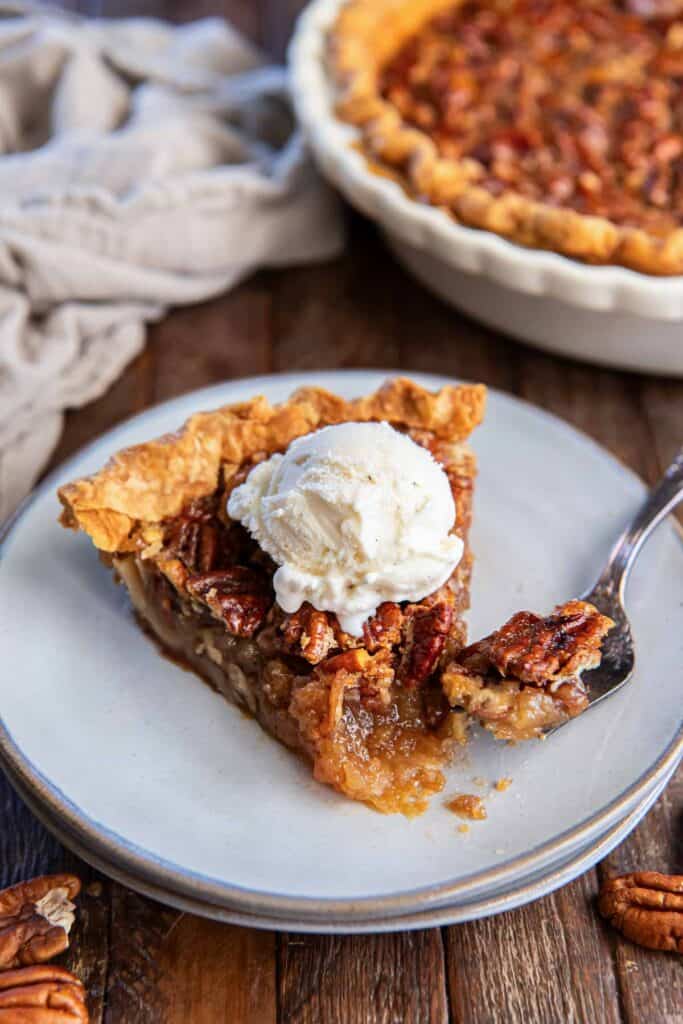 A fork resting on a plate next to a slice of bourbon pecan pie with vanilla ice cream.