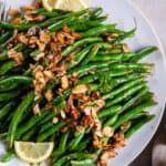 Green beans almondine on a white platter with lemon slices.