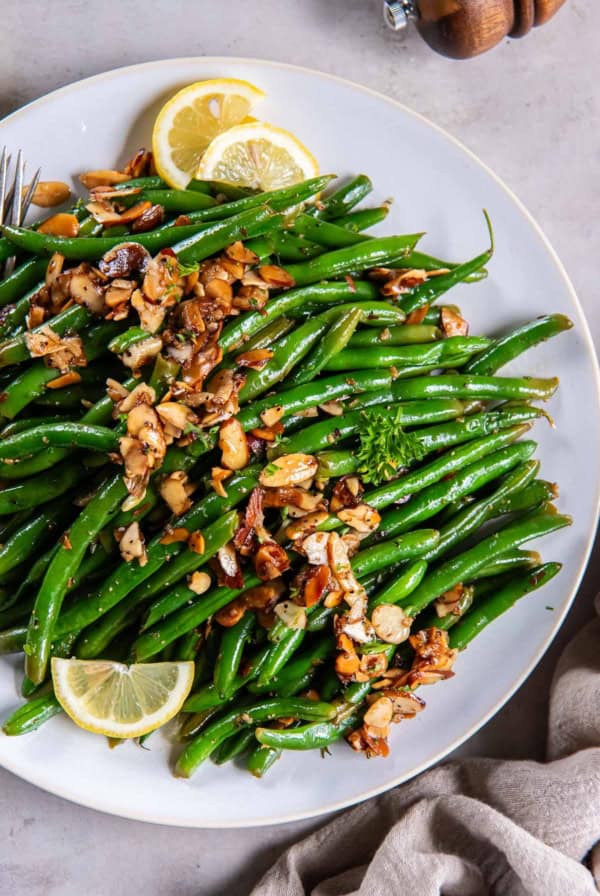 Green beans almondine on a white platter with lemon slices.