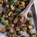 A wooden spoon scooping roasted brussels sprouts from a baking sheet.
