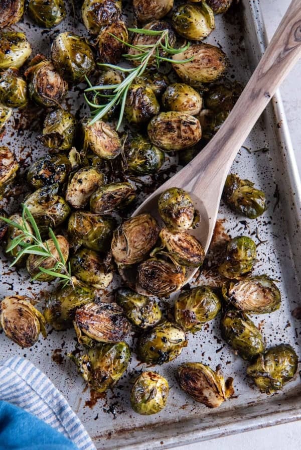 A wooden spoon scooping roasted brussels sprouts from a baking sheet.
