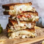 A sliced turkey pesto sandwich stacked on a wood board.