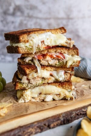 A sliced turkey pesto sandwich stacked on a wood board.