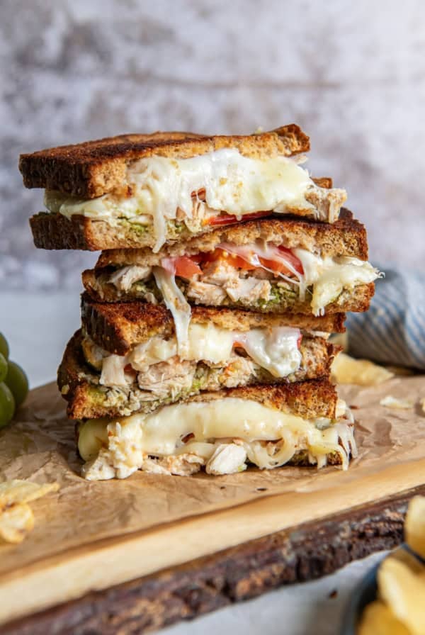 A sliced turkey pesto sandwich stacked on a wood board.