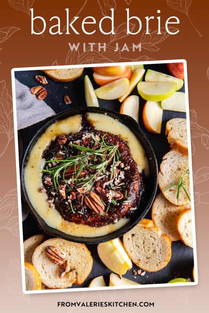 Crostini and apple slices surrounding baked brie with jam in a cast iron skillet with text overlay.