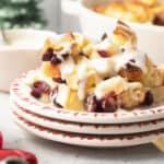 A plate with a serving of Christmas bread pudding with apples and cranberries topped with rum cream sauce on a kitchen counter.