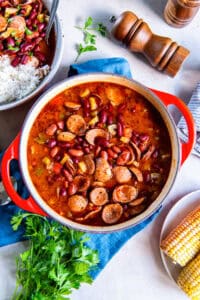 Red beans with sausage in a Dutch oven next to a pepper shaker and corn on the cob.