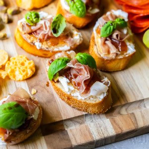 Goat cheese crostini with fig and prosciutto on a wood board.