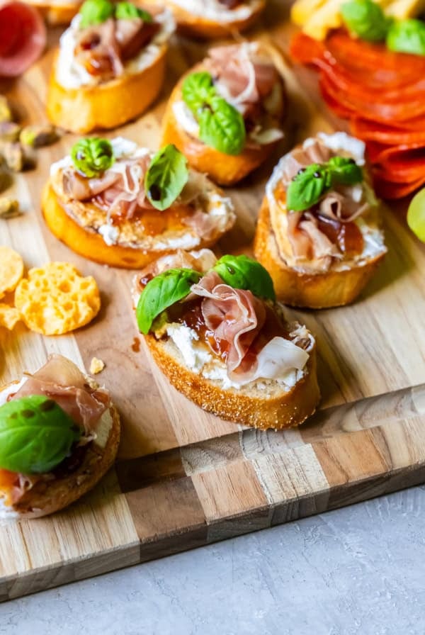 Goat cheese crostini with fig and prosciutto on a wood board.