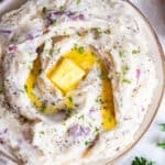 Red skinned mashed potatoes topped with butter in a white bowl.