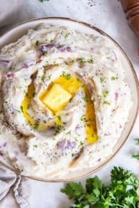 Red skinned mashed potatoes topped with butter in a white bowl.