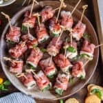 A platter filled with prosciutto wrapped mozzarella next to a bowl of marinated mozzarella balls.